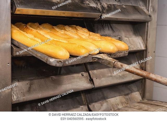 Baker taking out fresh baked bread from the industrial oven