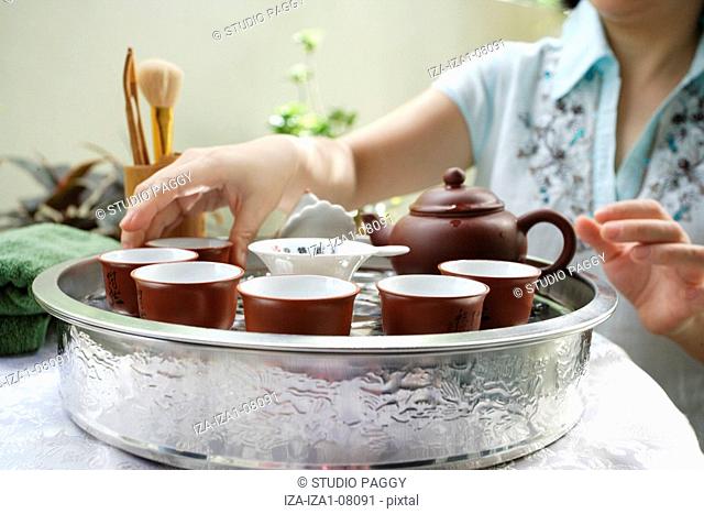 Mid section view of a mid adult woman arranging tea cups in a serving tray
