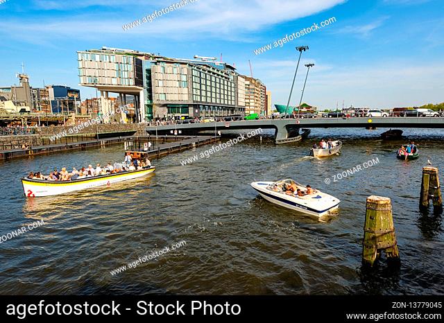 Amsterdam, Netherlands - 22 April 2019: Tourists in boats sightseeing in front of DoubleTree Hilton hotel, around the Central railway Station of Amsterdam