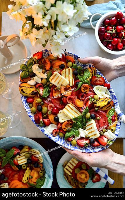 Tomato halloumi and peach salad on a platter Hands in the frame Dinner