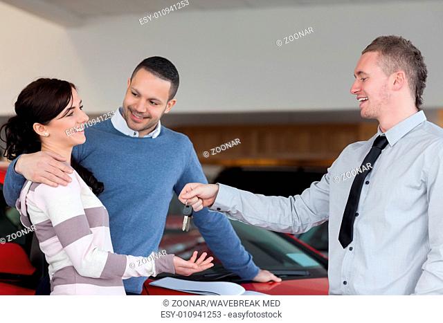 Couple embracing while receiving keys from a salesman