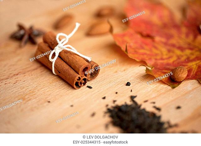cooking, spice and ethnoscience concept - cinnamon, maple leaf and almond on wooden board