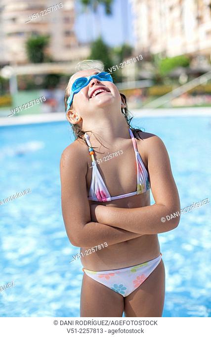 Pretty young girl in swimming pool laughing with Swim Goggles