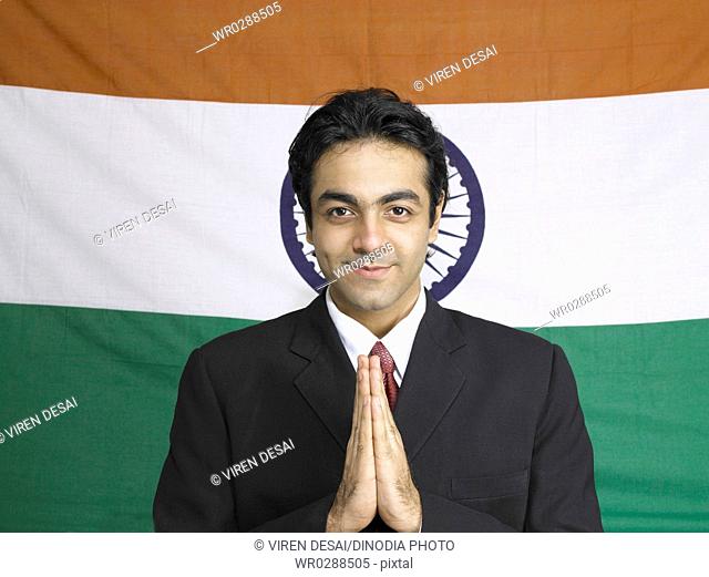 South Asian Indian executive in welcome pose standing in front of flag of India in background MR702A