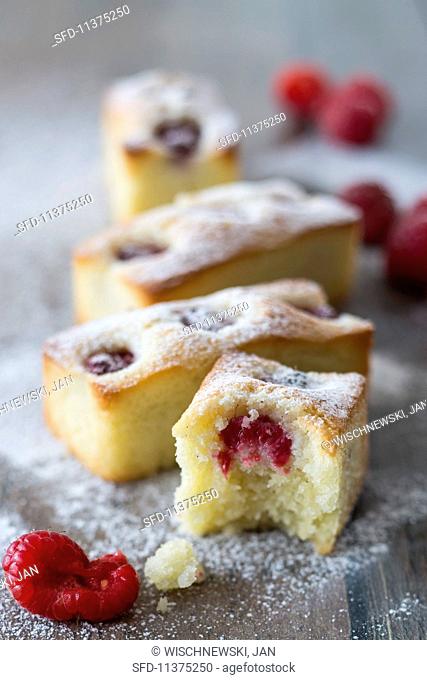 Financiers with raspberries and icing sugar, one with a bite taken out
