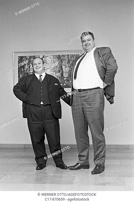 Seventies, black and white photo, humour, people, contrast, a runtish man and a large-sized man stand side by side, dwarf and giant, aged 30 to 40 years