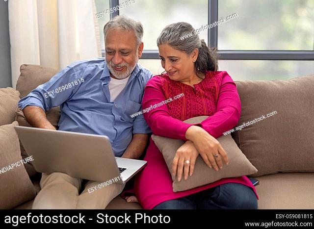 A SENIOR COUPLE SITTING TOGETHER AND HAPPILY USING LAPTOP