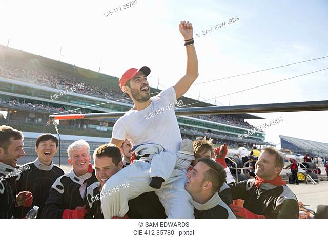 Formula one racing team carrying cheering driver on shoulders, celebrating victory on sports track