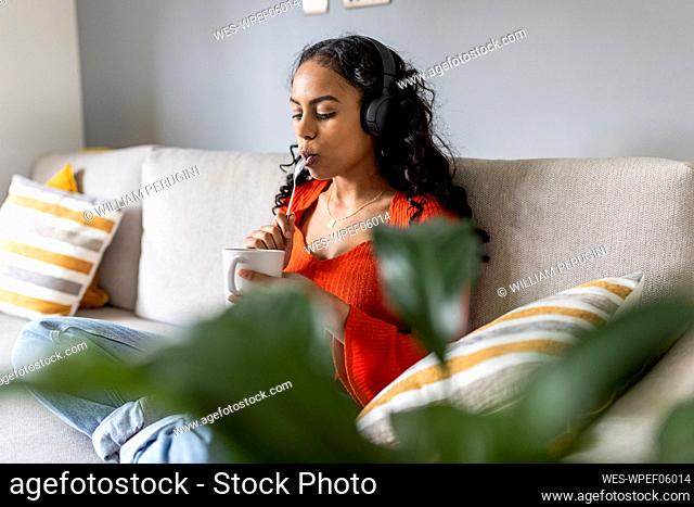 Woman licking spoon and listening music with headphones at home