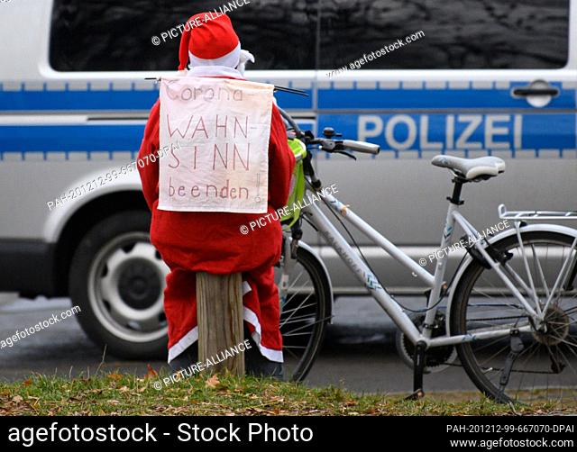 12 December 2020, Saxony, Dresden: A cyclist dressed as Santa Claus carries a banner ""End Corona Madness!"" on his back and sits on a wooden pole on the...