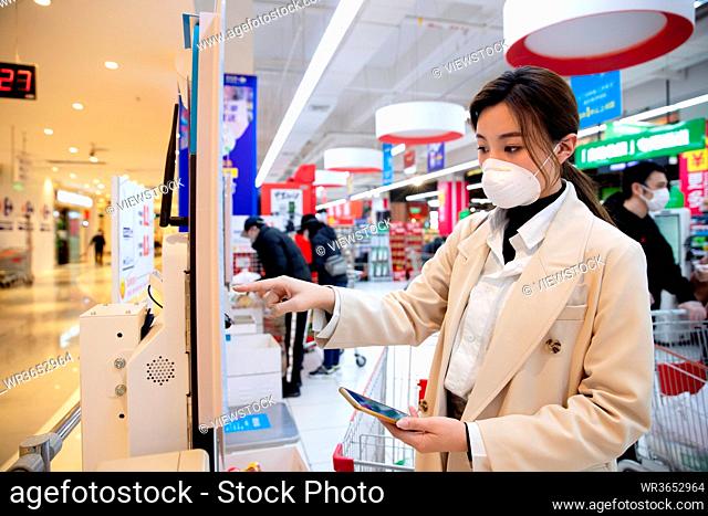 Wearing a mask of the young woman in the supermarket pay by phone