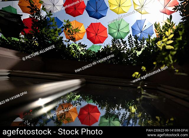 PRODUCTION - 20 June 2023, Rhineland-Palatinate, Mainz: Umbrellas from the ""Umbrella Sky"" campaign are reflected in a window pane in the old town