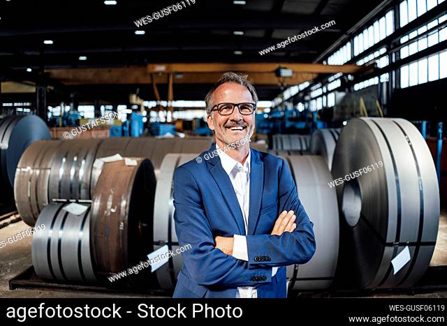 Smiling male professional standing with arms crossed in industry