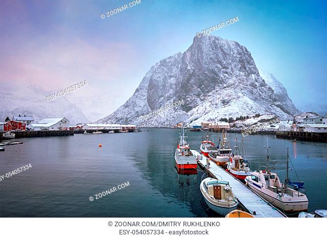 Pier with ships in Hamnoy fishing village on Lofoten Islands, Norway with red rorbu houses. With falling snow