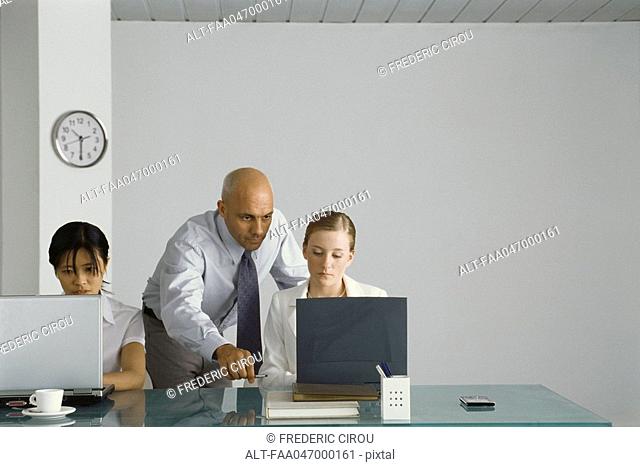 Professional man standing behind young female colleague, pointing at her computer screen