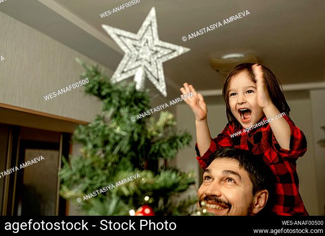 Happy son screaming looking at Christmas tree with father at home