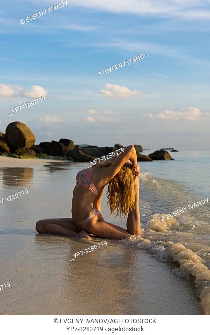 Thai beach yoga - girl in pigeon pose on Ko Lipe island, Thailand