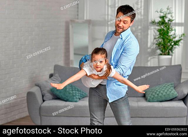 Happy little child girl flying in dads arms at home. family having fun