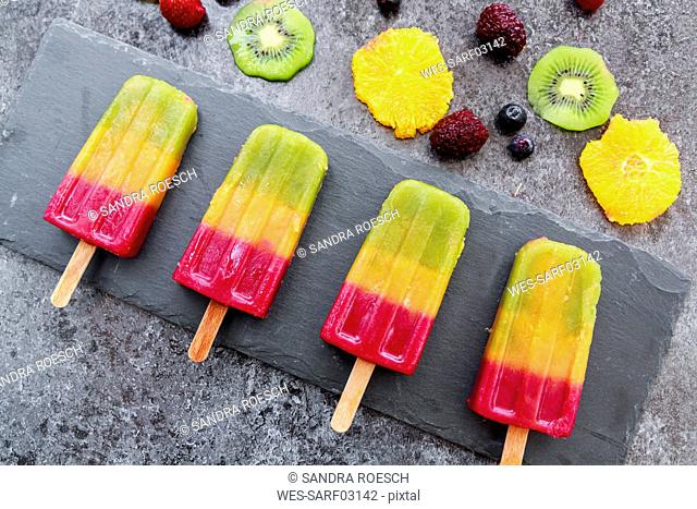 Row of four homemade fruit smoothie ice lollies on slate