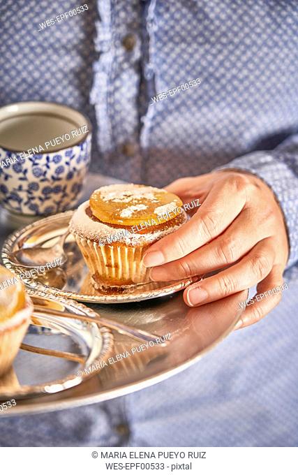 Woman's hand holding muffin with candied orange slice on silver platter
