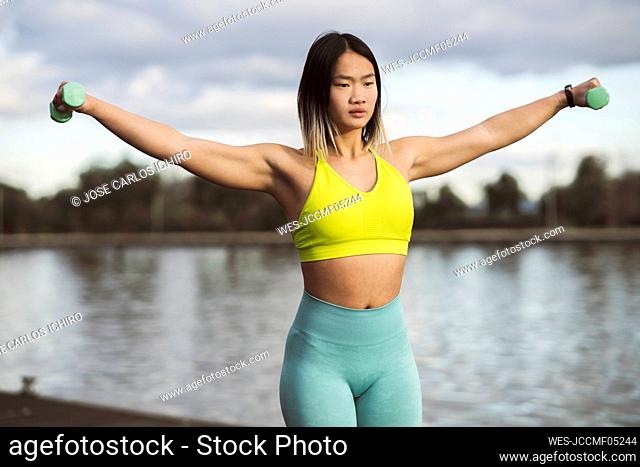 Young athlete exercising with dumbbells by lake