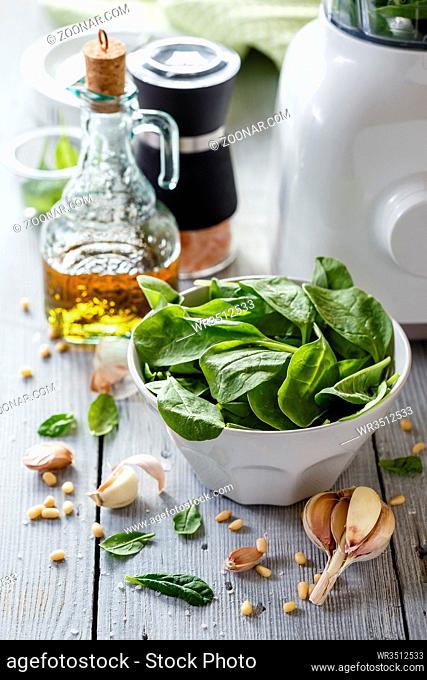 Spinach pesto: spinach leaves, garlic, pine nuts, salt and olive oil on white wooden background