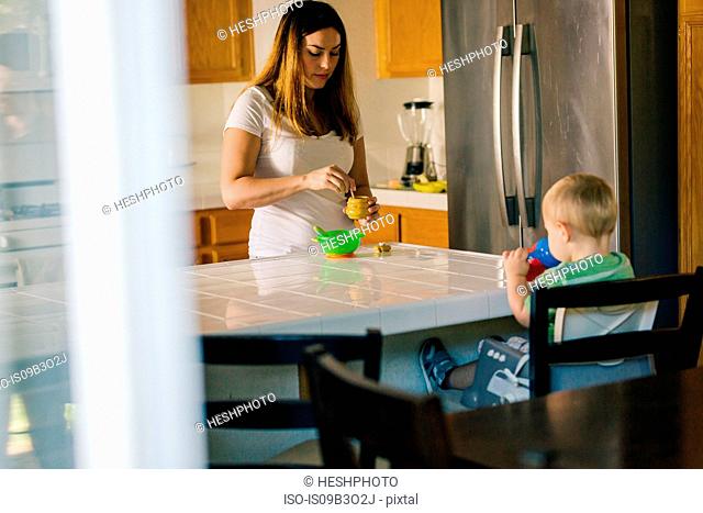 Mother and young son at kitchen table, mother preparing food, son drinking from sippy cup