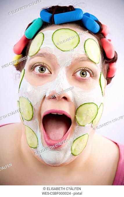 Portrait of screaming woman wearing curlers and beauty mask with slices of cucumber
