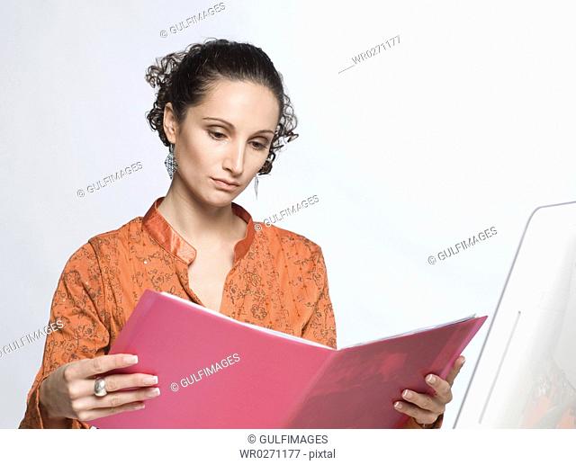 Young woman sitting by computer, reading book