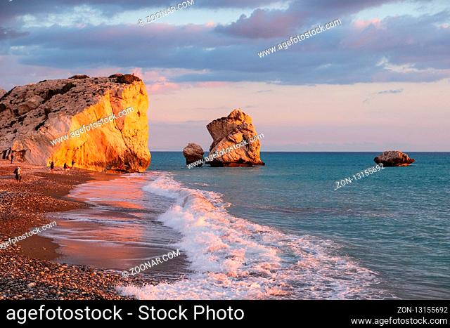 Paphos, Cyprus - November 24, 2018: People enjoy themselves at the beach againt the Petra tou Romiou rocks bathed in afternoon light, in Paphos, Cyprus