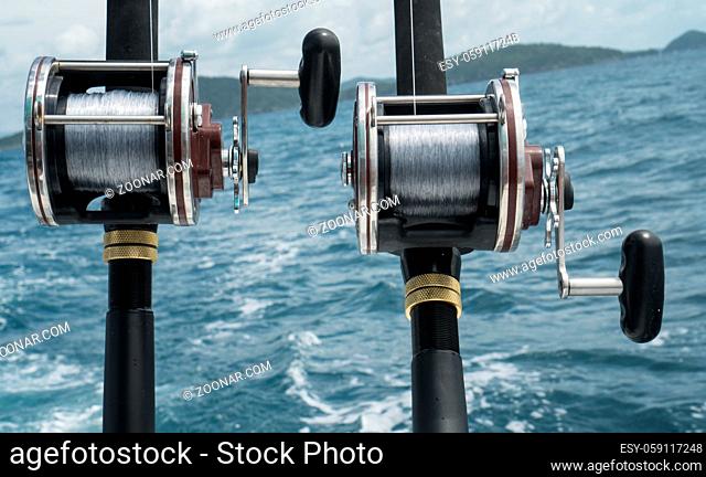 Fishing rods on a boat over blue sea and sky. Picture of two fishing rods in pole holders on the back of a boat