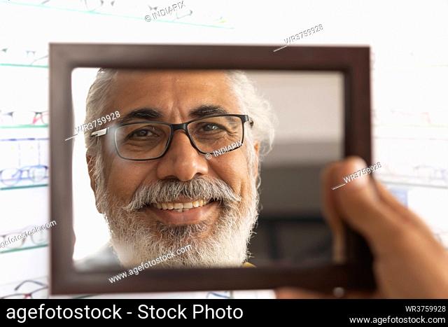 A HAPPY OLD MAN LOOKING AT MIRROR WHILE TRYING ON NEW SPECS