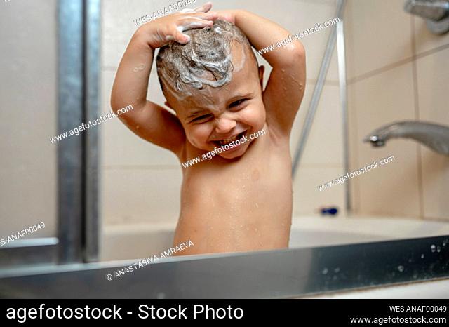 Happy baby boy washing hair in bathtub
