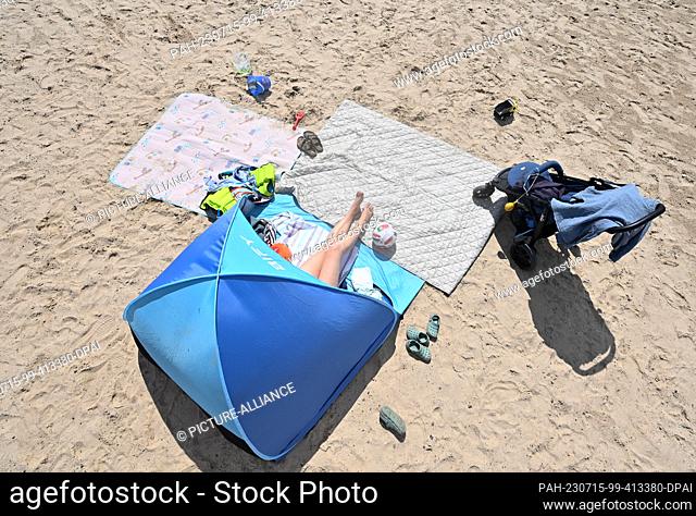 15 July 2023, Timmel: A woman enjoys the summer weather at a swimming lake in her sun shell. Weekend vacationers and tourists have sought cooling on the coasts...