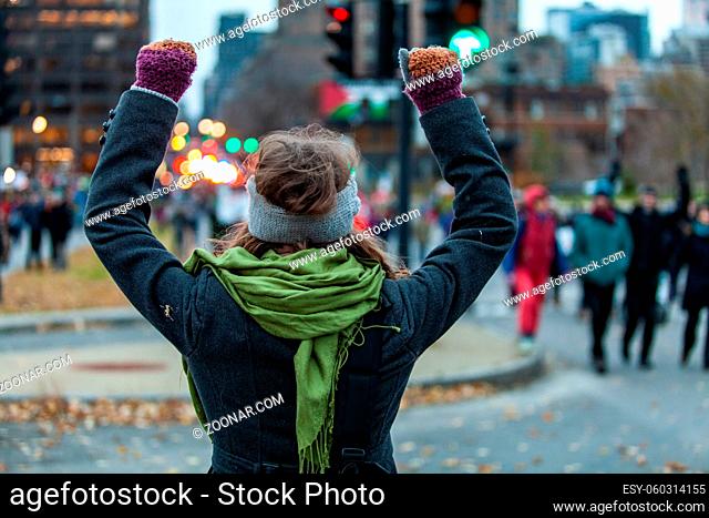 Young woman is raising her arms high while looking at the crowd during an ecological protest. Shot from the back