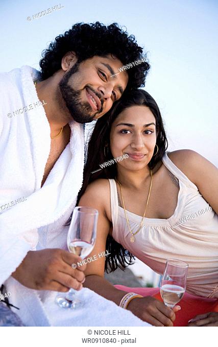 Couple sitting outdoors with champagne flutes and scenic background smiling and snuggling