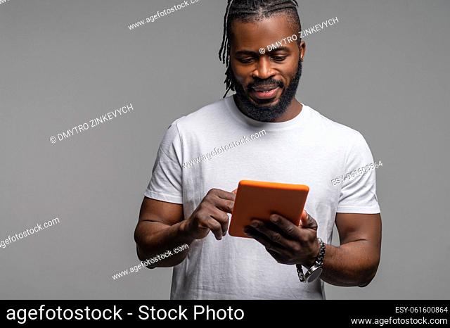 Waist-up portrait of a calm focused young male looking at the tablet in his hands