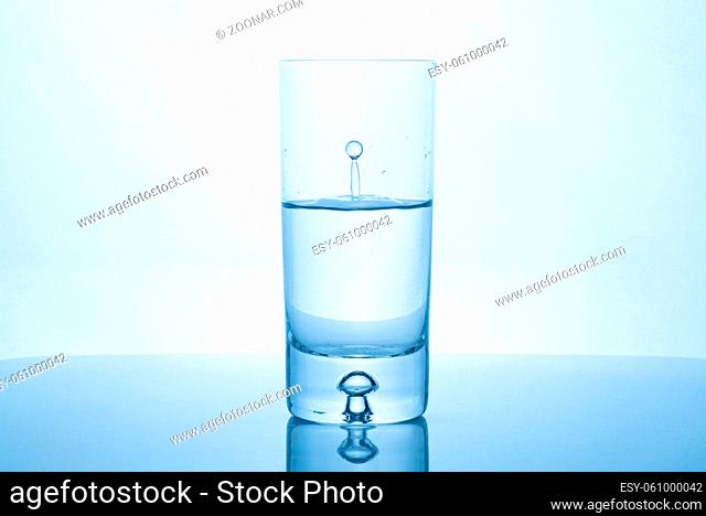 Water drop splash inside glass half full against bright background. Purity and health concept