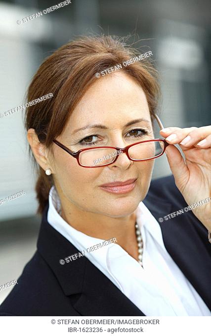 Business woman, years 45, wearing a lady's suit and frowning suspiciously over the top of her glasses