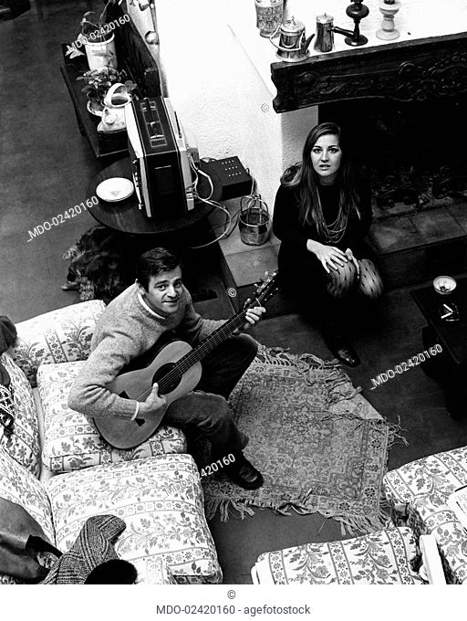 The Italian songwriter Sergio Endrigo is playing guitar next to his wife Lula in the living-room of their house. Casali di Mentana, Rome, Italy, 1968