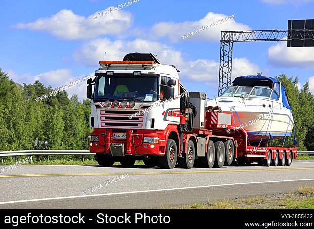 Red white Scania semi trailer of Vuorsola Oy transports recreational boat on highway 2 on a day of summer. Forssa, Finland. July 31, 2020