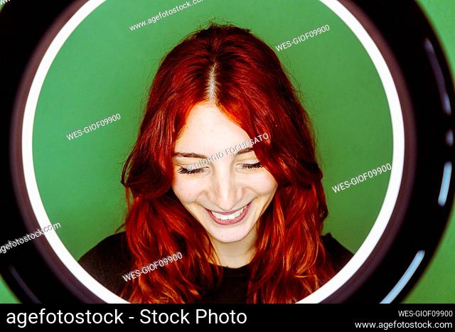 Smiling redhead woman with ring flash light standing against green background