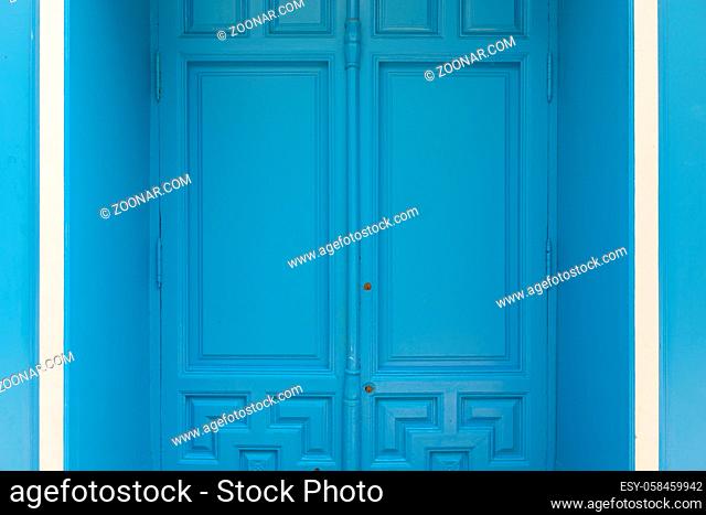 Portrait of blue painted door with white details on side in concrete wall