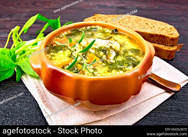 Pork ribs soup with couscous and spinach in a clay bowl on napkin, bread on wooden board background