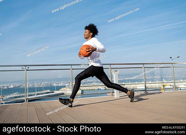 Athlete running with basketball on pier at sunny day