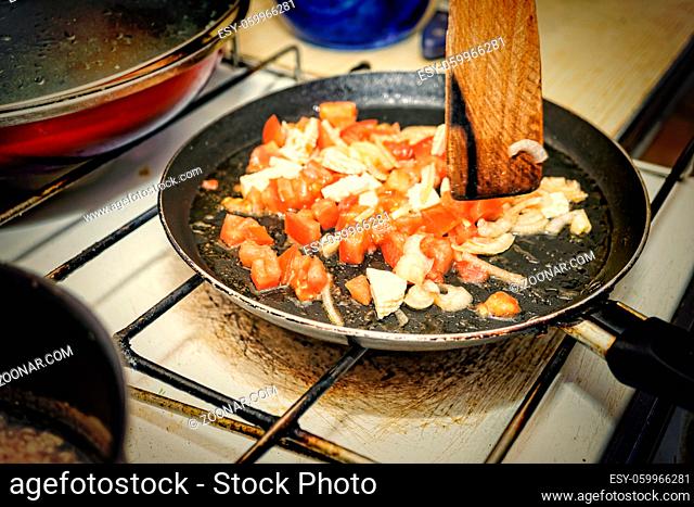 Woman preparing breakfast at home kitchen. Roasting vegetables in a pan with tofu and cherry tomatoes