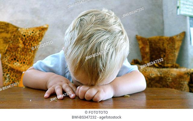 little boy with blond hair falling asleep at a desk