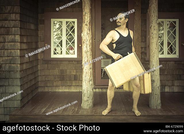 Goofy gentleman dressed in 1920’s era swimsuit holding suitcases on porch of cabin