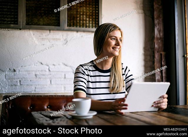 Smiling woman using digital tablet while looking away in cafe