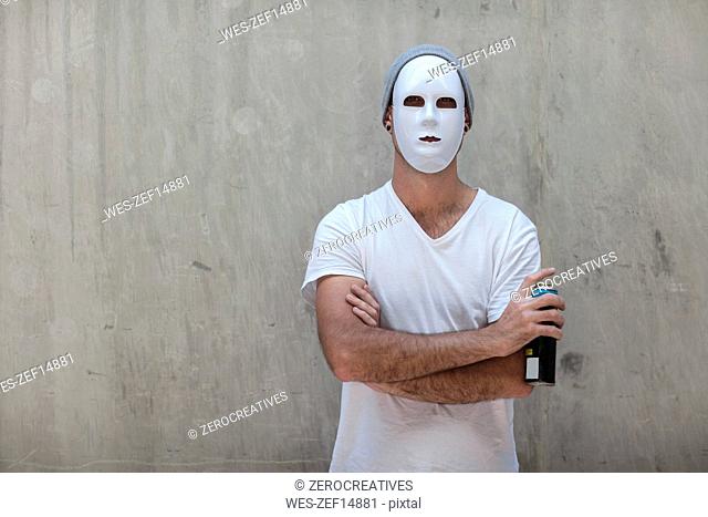 Man wearing a mask standing next to a concrete wall holding a can of spray paint